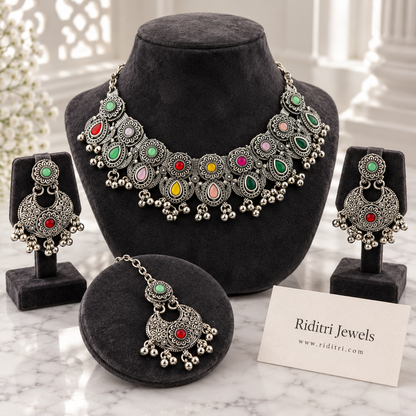 Navratan oxidised necklace set with multicolour stones, floral motifs and ghungroo drops, with matching chandbali earrings and maang tika by Riditri