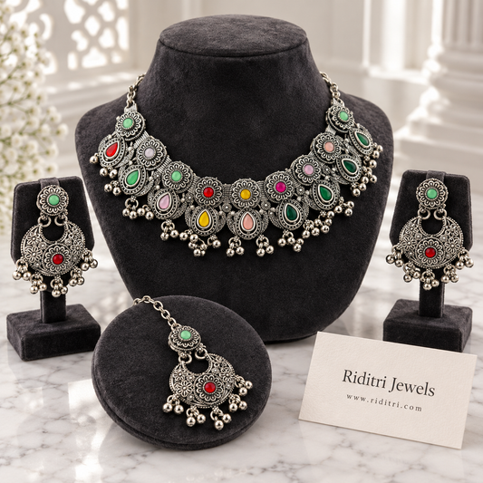 Navratan oxidised necklace set with multicolour stones, floral motifs and ghungroo drops, with matching chandbali earrings and maang tika by Riditri