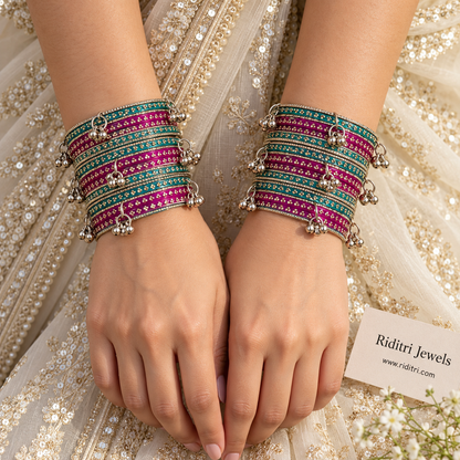 Rani pink and radium green glass bangles stacked with silver ghungroo bangles on display stand